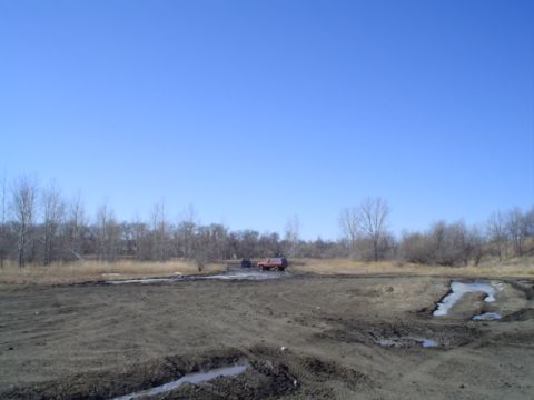 1981 Ford Bronco - A red SUV is stuck in a muddy area under a clear blue sky.