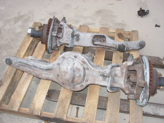 Two old, dusty vehicle axle assemblies with brake rotors are sitting on wooden pallets