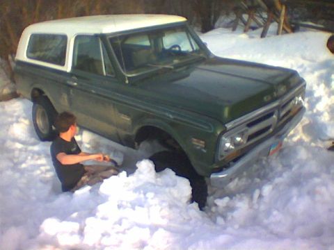 1979 Ford Bronco - A GMC K5 Blazer is stuck in the snow, with a person sitting next to the front tire.