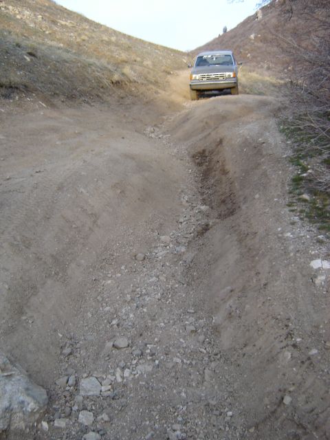 1991 Ford Bronco - A 1991 Ford Bronco navigates a steep, rocky dirt path on an off-road trail.