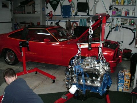 1978 Ford Mustang II - A red 1978 Ford Mustang II, identified by its "KING COBRA" badging, is shown in a garage with its engine being removed by an engine hoist.