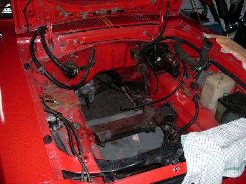 1978 Ford Mustang II - Engine bay of a red car, missing its engine, showing brake booster and wiring.