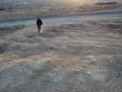 1991 Ford Bronco - A person walks across a bumpy dirt terrain, with a road and distant buildings visible in the background.