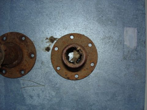 1987 Ford Bronco - Close-up of two corroded metal flanges, each with multiple bolt holes, on a textured background.