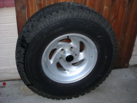 1987 Ford Bronco - Spare tire and rim shown leaning against a wooden fence.