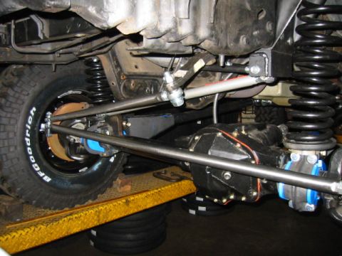 1992 Ford Bronco - Underside view of a lifted solid-axle front suspension showing a black-painted differential housing, tall coil springs, blue polyurethane-c…