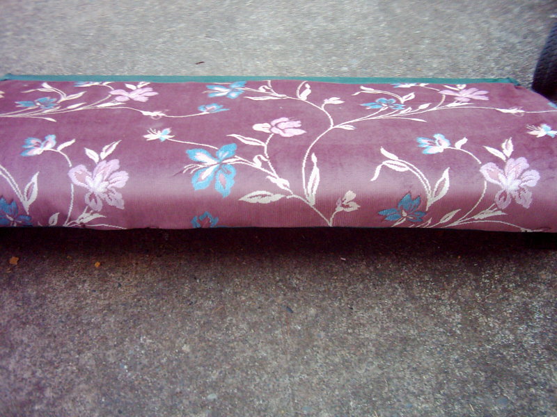 Floral upholstered seat cushion with purple and pink flowers on a concrete surface
