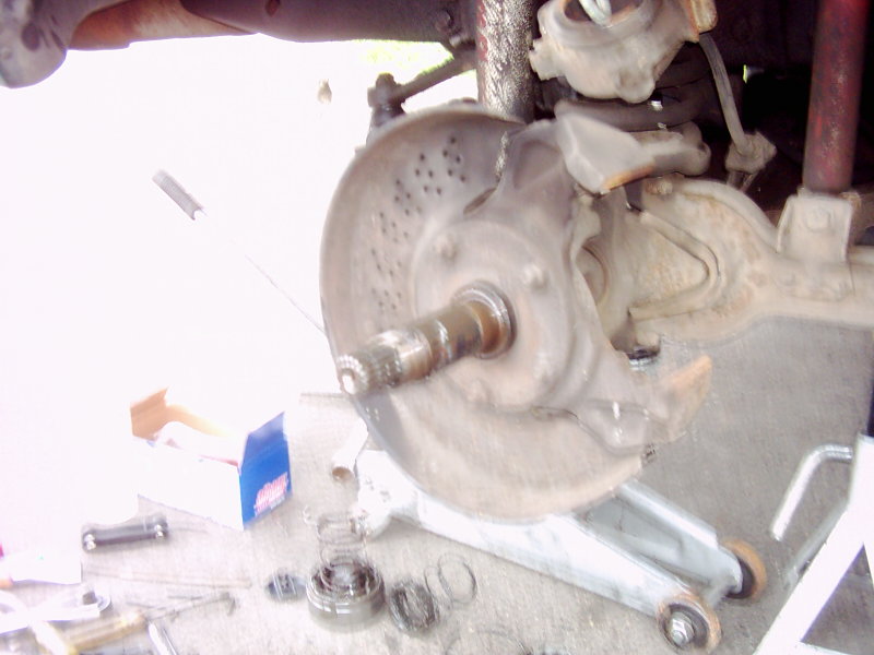 Close-up of a vehicle's front brake rotor and hub assembly, with tools and parts scattered on the ground