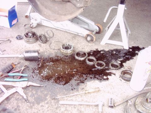 1978 Ford Bronco - Disassembled vehicle wheel hub and bearings are laid out on the ground next to tools and a jack stand.
