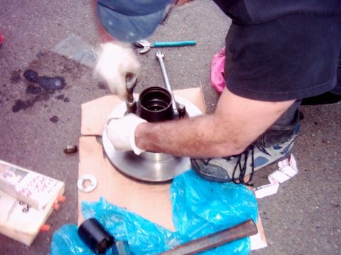 1978 Ford Bronco - Mechanic working on a brake rotor and hub assembly on the ground.