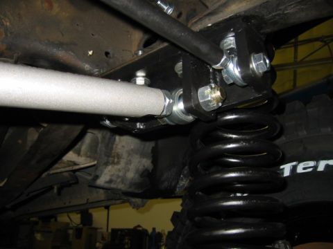 1992 Ford Bronco - Underbody close-up of a black double-shear steel bracket bolted to the frame with large zinc-plated bolts and nuts, anchoring the upper end…