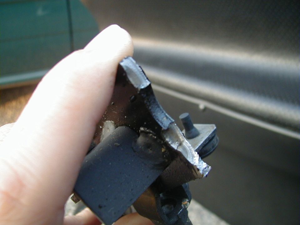Broken black car part held in a hand, with a metallic car door in the background
