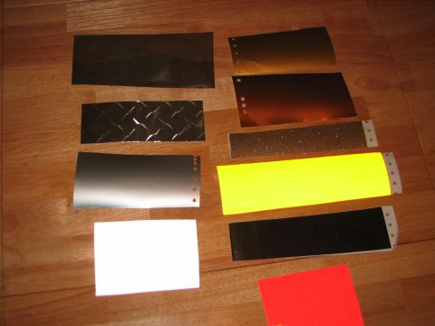 2002 Ford Taurus - Swatches of reflective material laid out on a wooden surface. Includes diamond plate, yellow, black, white, and metallic finishes.
