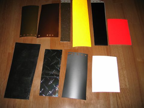 2002 Ford Taurus - Ten rectangular vinyl wrap and decal samples laid out on a light hardwood floor, including gloss black, brushed graphite, chrome diamond-pl…