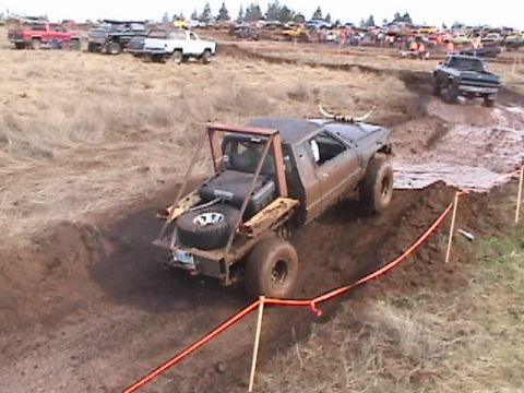 1994 Ford Explorer - A heavily modified pickup truck, adorned with bull horns, tackles a muddy obstacle course during an event.