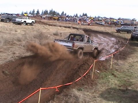 1994 Ford Explorer - A tan SUV navigates a muddy obstacle course, kicking up a cloud of dust and dirt.