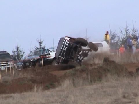 1994 Ford Explorer - An off-road vehicle has overturned in a mud pit during an event, with other vehicles and people in the background.