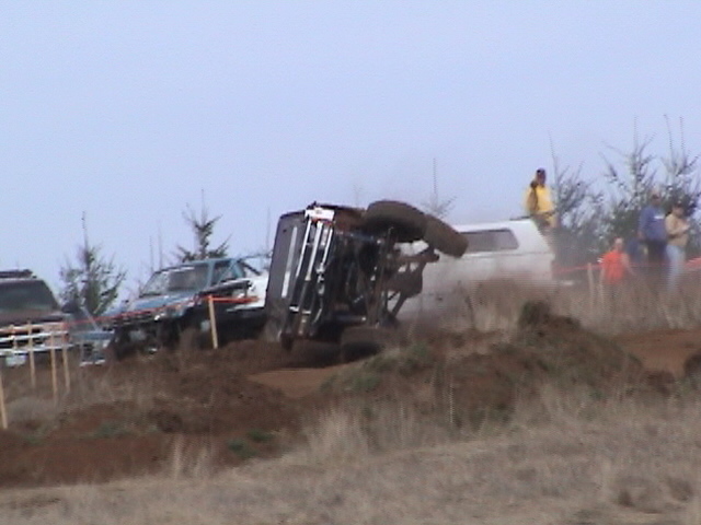 Off-road vehicle flipped on its side with another vehicle nearby and people watching