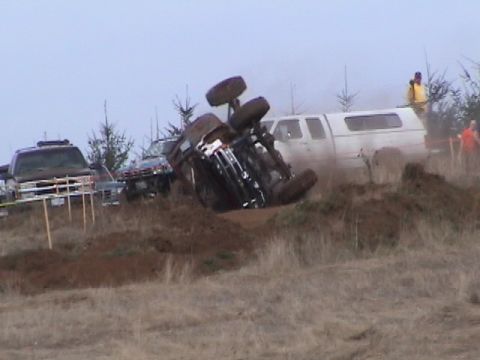 1994 Ford Explorer - An SUV has overturned during a mud festival event, with other vehicles and spectators visible in the background.