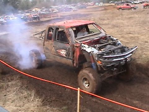 1994 Ford Explorer - A heavily modified pickup truck navigates a muddy track, emitting smoke from its tires.