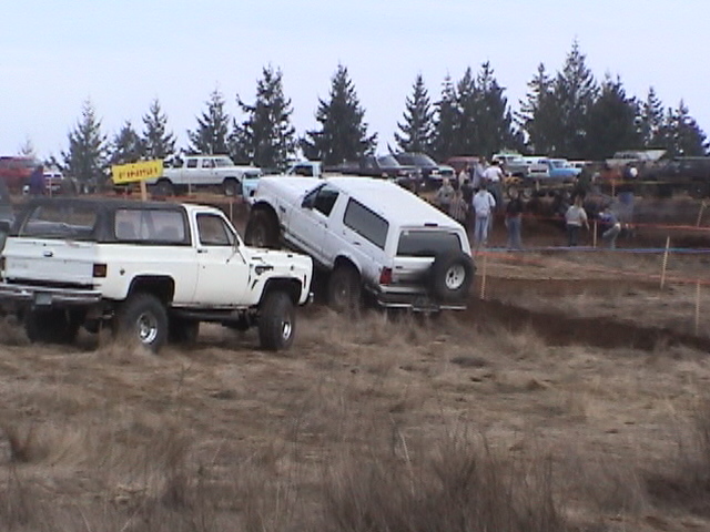 White SUV with spare tire on rear is stuck in mud next to a white pickup truck