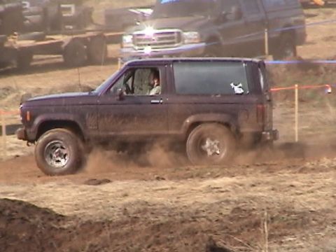 1994 Ford Explorer - A dark purple SUV navigates a muddy off-road course, with another vehicle visible in the background.