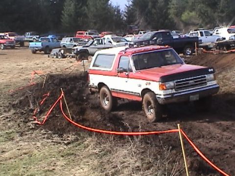1994 Ford Explorer - A red and white SUV navigates a muddy off-road course with other vehicles visible in the background.
