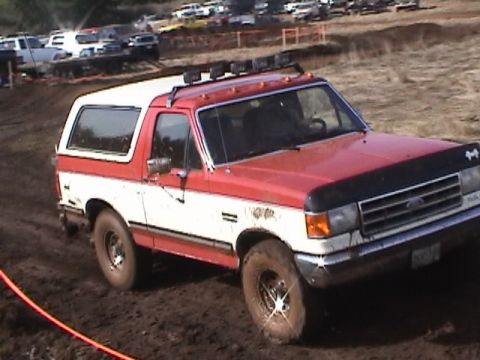 1994 Ford Explorer - This two-door SUV, likely from the late 1980s, navigates a muddy terrain with its roof rack and off-road tires.