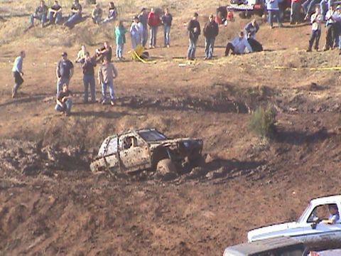 1994 Ford Explorer - An off-road event shows a vehicle deeply stuck in mud, with spectators observing the scene from a nearby embankment.