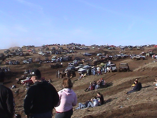 Spectators on a brown hillside watching trucks at an off-road hillclimb event