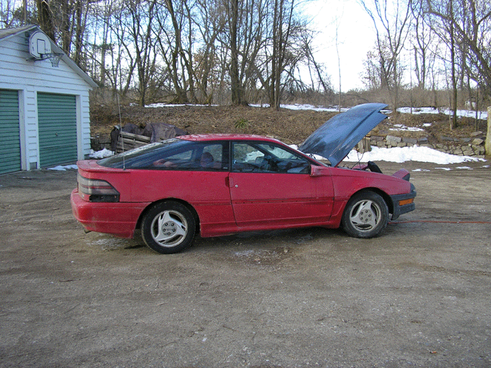 red hatchback car with hood open, parked outside near a building