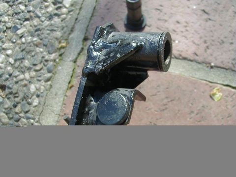 1993 Ford Probe - A close-up view of a damaged black metal automotive component resting on a brick and gravel surface.