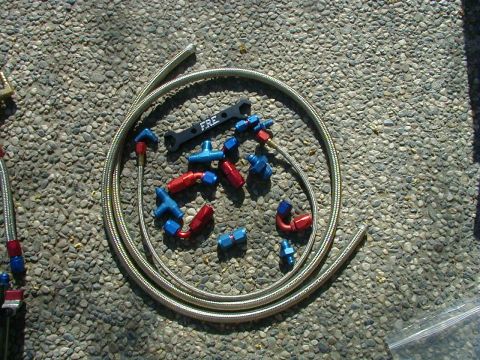 1993 Ford Probe - A collection of braided fuel lines and assorted fittings are laid out on a gravel surface.