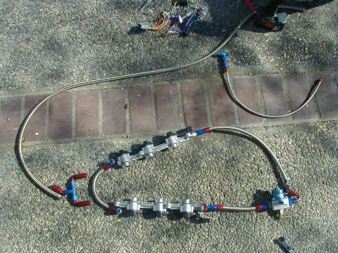 1993 Ford Probe - A disassembled fuel rail system with braided lines and fittings lies on a paved surface.