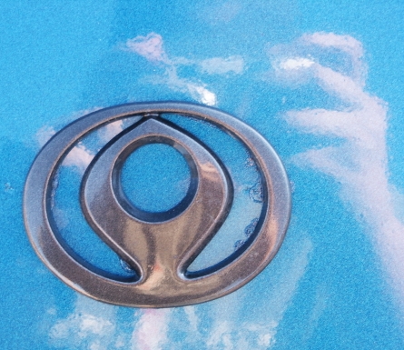 1993 Mazda MX-6 - A close-up view of the Mazda emblem is shown against a bright blue background with a watermark at the bottom.