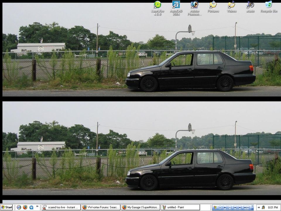 Black sedan parked on a roadside with weeds and a chain-link fence