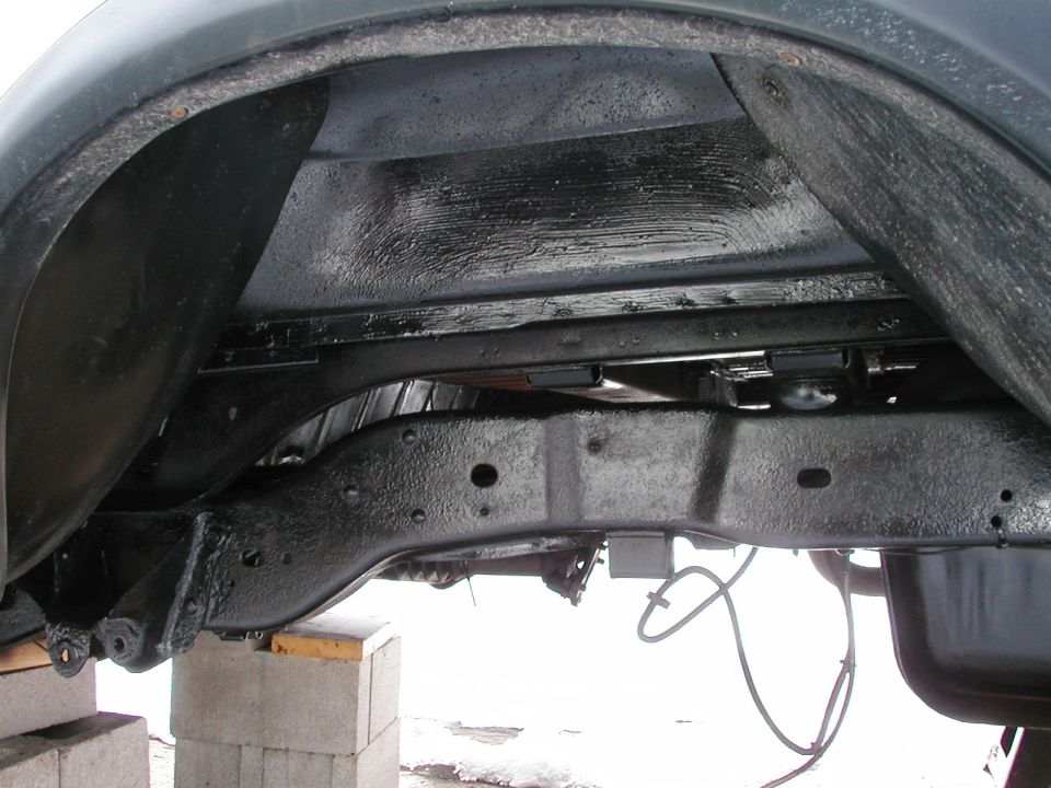 Close-up of vehicle frame and suspension parts, possibly from a truck or SUV, with black protective coating