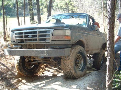 1993 Ford Bronco - This 1993 Ford Bronco is shown off-roading on a dirt path with trees in the background.