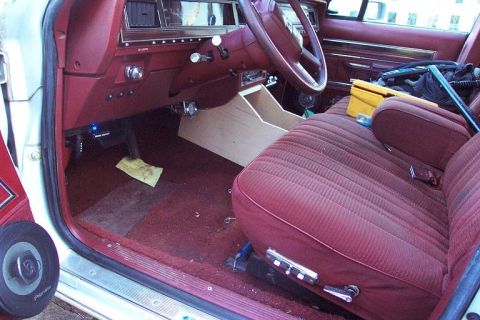 1985 Ford Crown Victoria LTD - The interior of a car shows maroon upholstery, a custom wooden center console, and various items on the passenger seat.