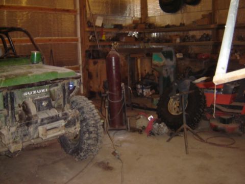 1992 Ford Bronco - A green Suzuki Samurai sits in a cluttered garage, showing its front end and winch.