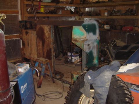 1992 Ford Bronco - A heavily rusted vehicle body sits in a cluttered workshop, showing signs of disrepair and ongoing work.