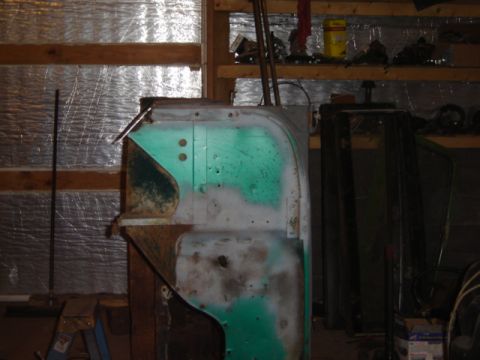 1992 Ford Bronco - A vehicle body panel, partially painted green and gray with visible rust, sits in a workshop.