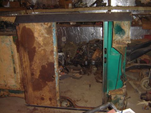 1992 Ford Bronco - A heavily rusted vehicle door frame is open, revealing a pile of engine parts and debris inside a workshop.