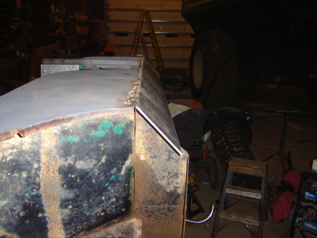 close-up of a rusty vehicle body panel being worked on, with a ladder and tire in the background