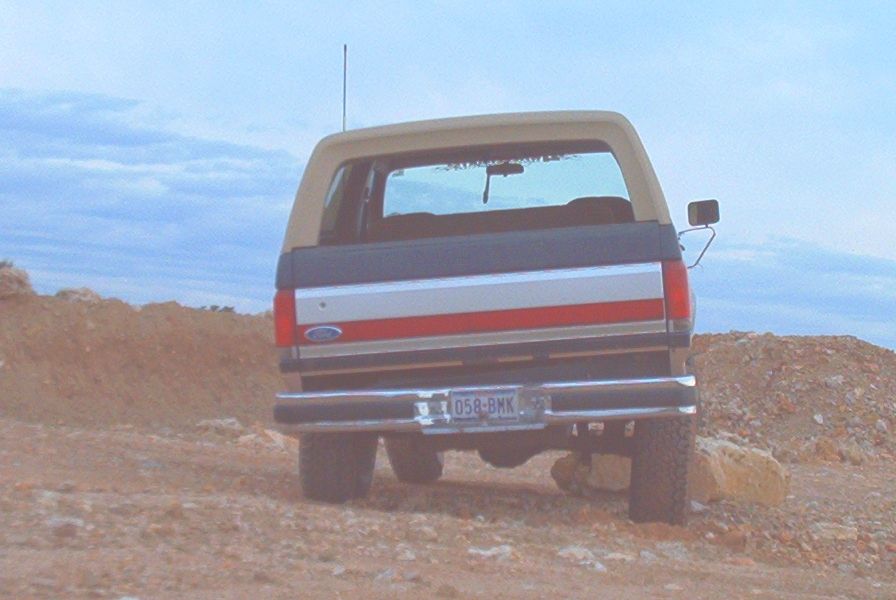 Rear view of a tan and dark blue 1989 Ford Bronco with red and silver stripes on tailgate
