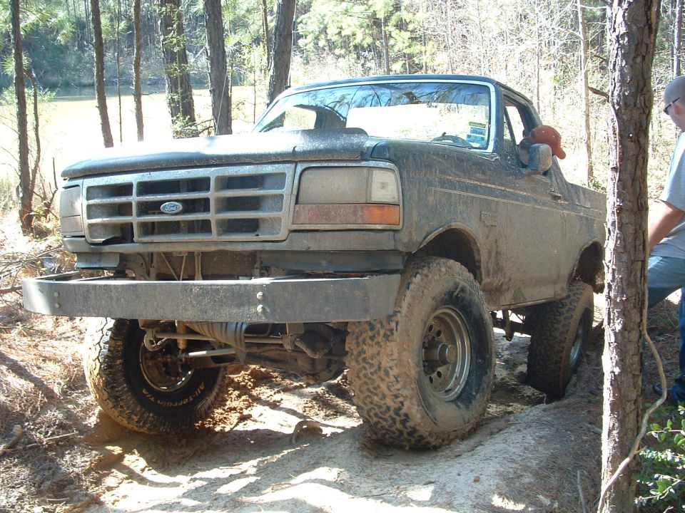 Mud-covered dark green 1992 Ford Bronco with aftermarket bumper and hood scoop, angled from the front-left