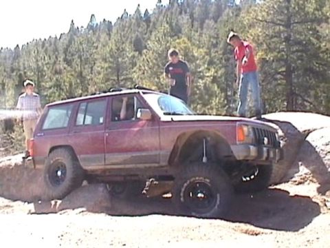 1993 Ford Bronco - This Jeep Cherokee XJ is attempting to climb over a rocky obstacle on a dirt trail.