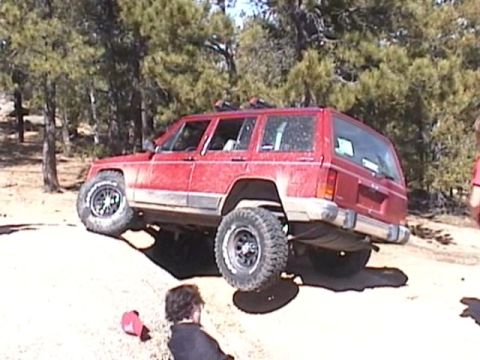 1993 Ford Bronco - A red Jeep Cherokee XJ navigates a challenging off-road course with one wheel lifted.