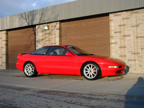 1994 Ford Probe - A red 1994 Ford Probe is parked in front of a building with large garage doors.
