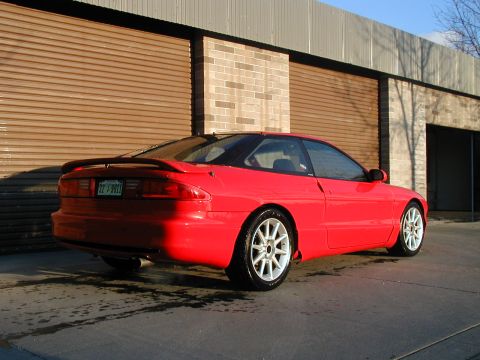 1994 Ford Probe - A red coupe with a spoiler and aftermarket wheels is parked outside a garage.